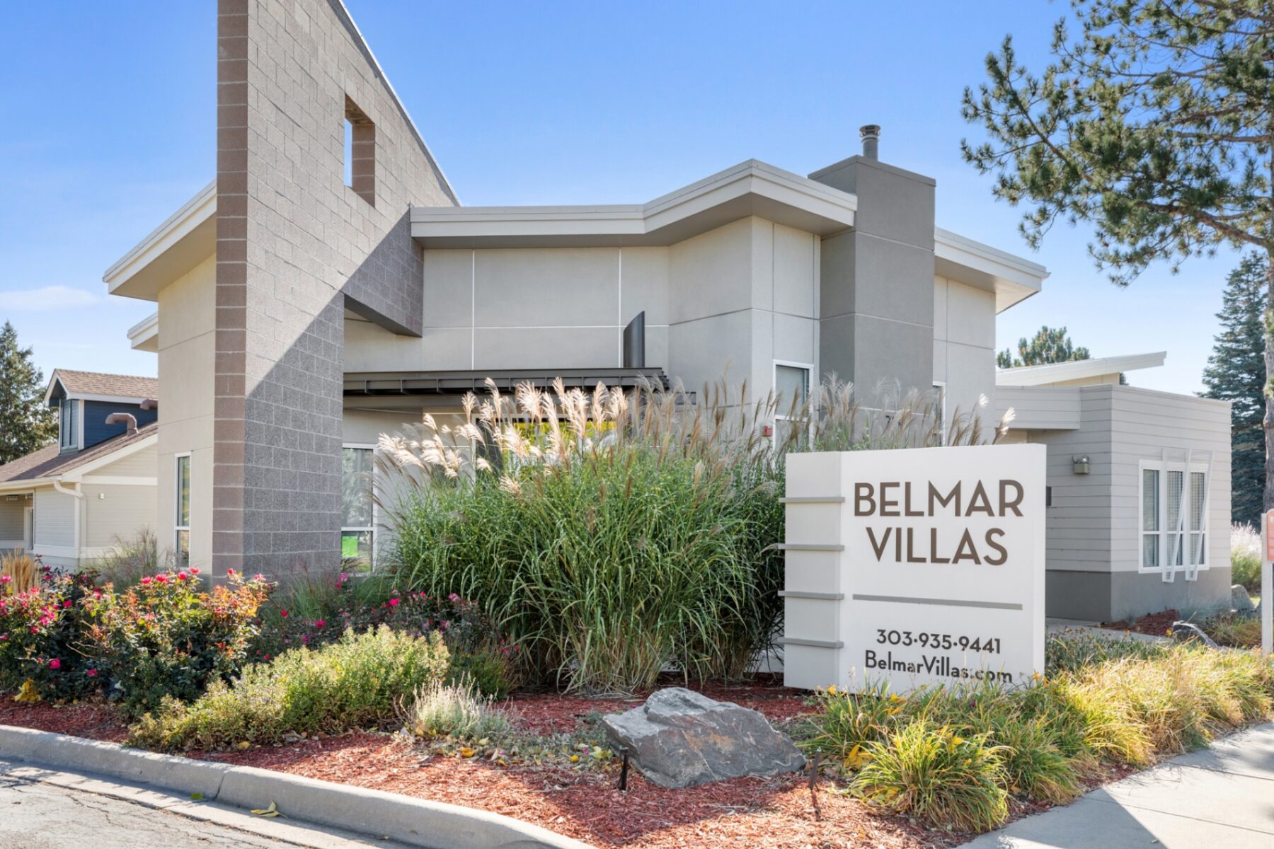 Exterior of leasing office with dense landscaping and monument sign for Belmar Villas