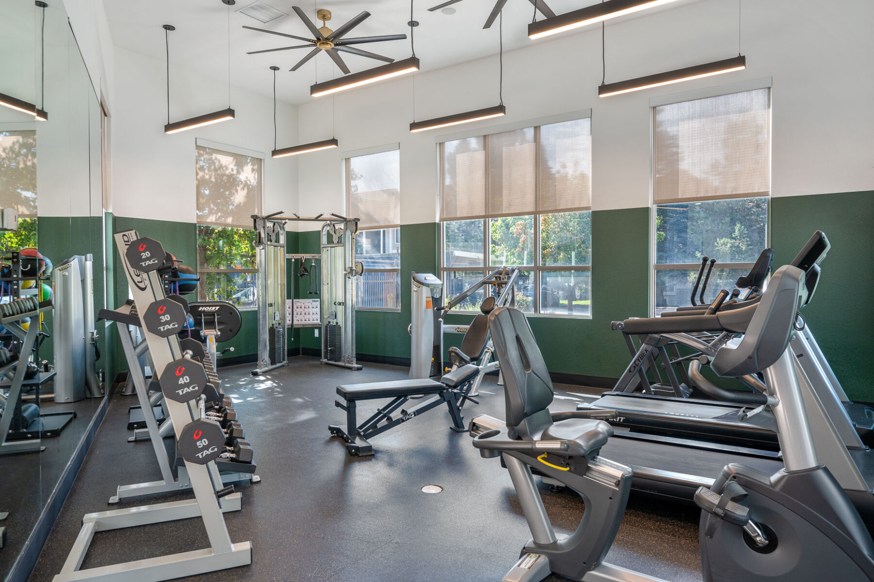 Fitness center with strength and cardio equipment in a space with mirror lined windows and overhead lighting