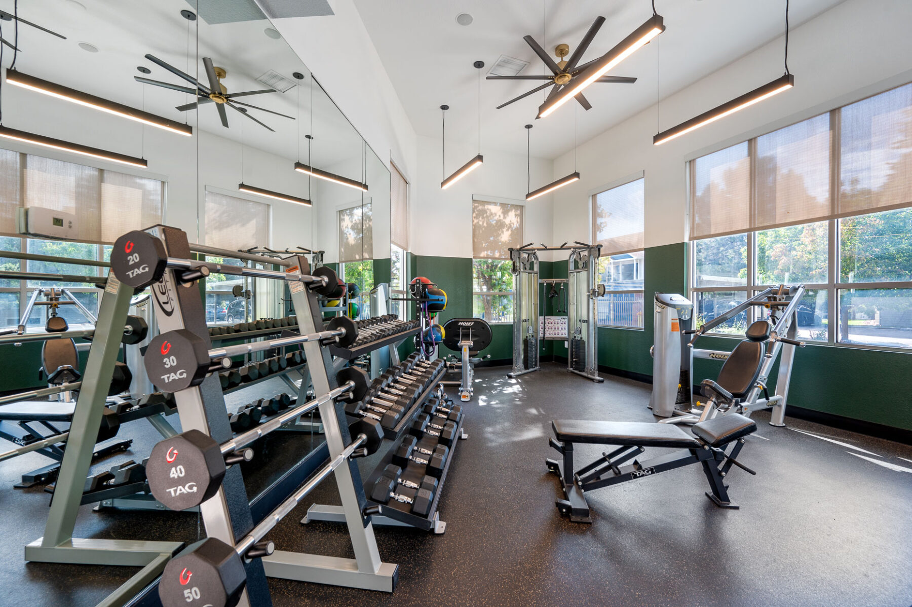 Fitness center with strength and cardio equipment in a space with mirror lined windows and overhead lighting