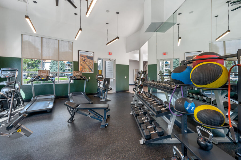 Fitness center with strength and cardio equipment in a space with mirror lined windows and overhead lighting