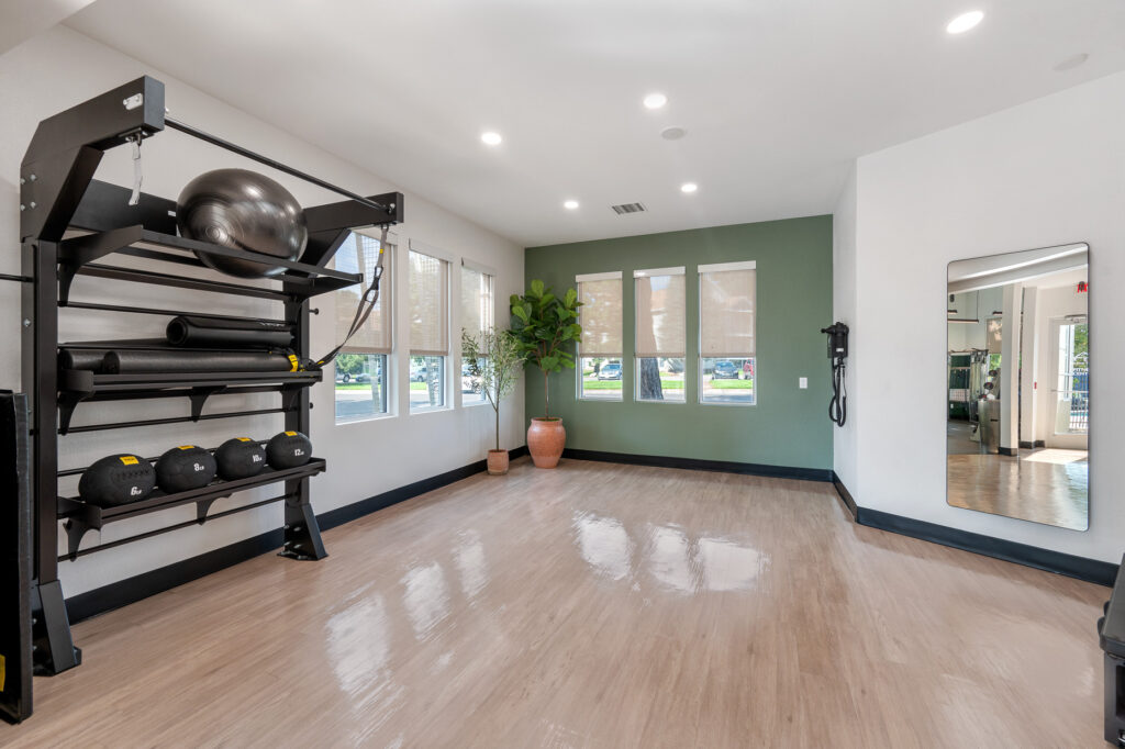 Fitness center studio space with strength training equipment, a mirror and natural lighting from windows