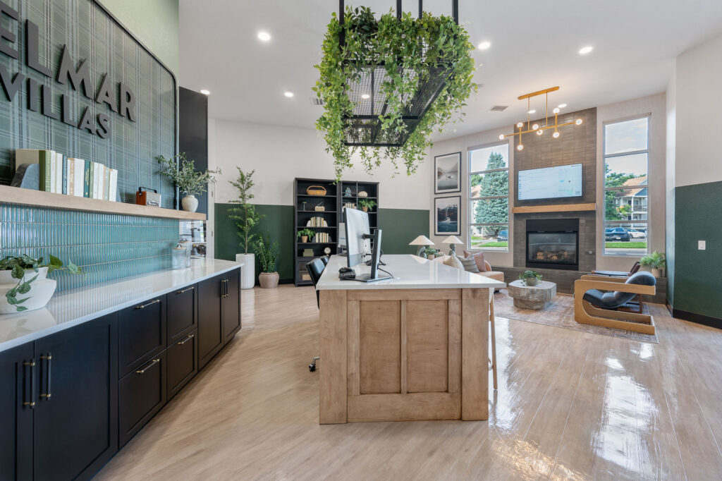 Leasing office entry space with reception space, bookshelf and ladder and armchairs and a sofa next to a television mounted above a fireplace