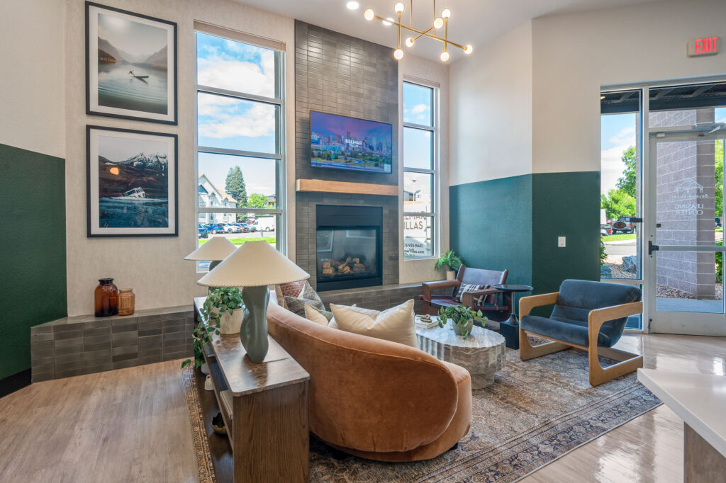 Leasing office entry space with armchairs and sofa seating next to a television mounted above a fireplace